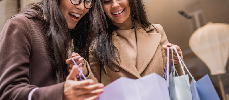 Woman showing her purchase to her friend, with both of them smiling and looking happy.