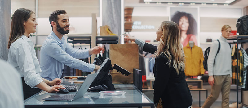 Store employee handing a paper bag to a customer after they have made a purchase.